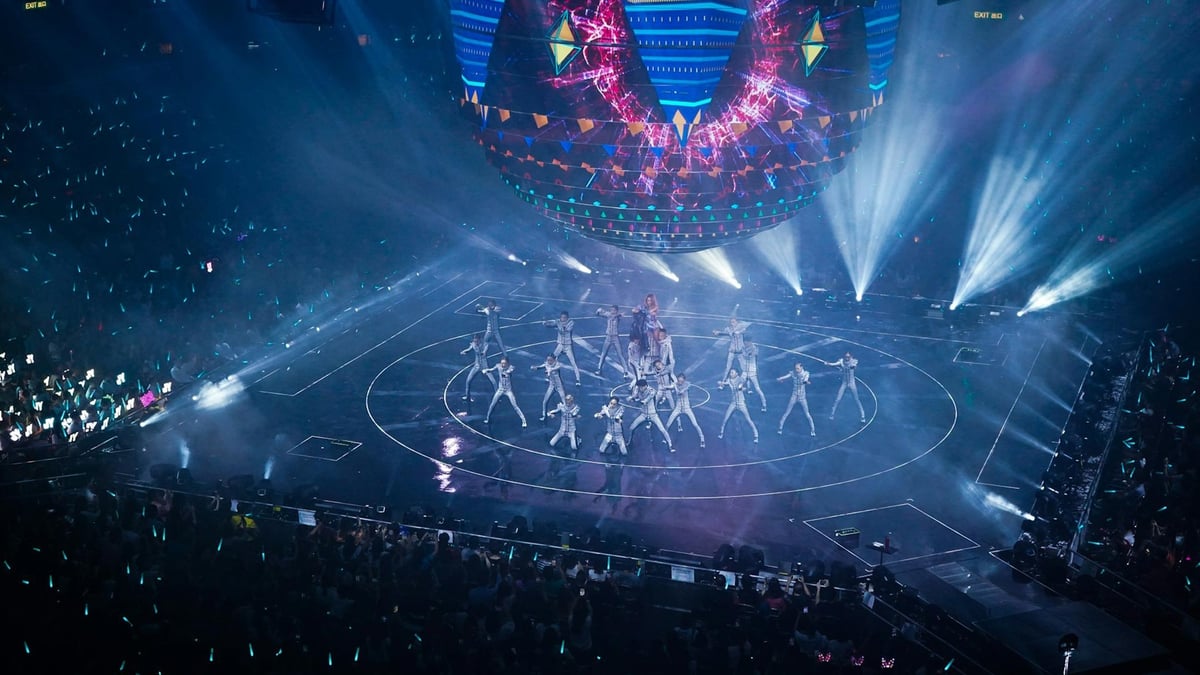 Esiintyjiä lavalla suuressa musiikkikilpailussa, näyttävä valoshow ja yleisö areenalla.