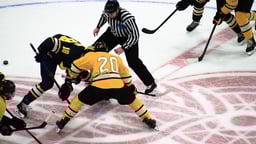 Jääkiekko-ottelun aloitustilanne, jossa pelaajat kamppailevat kiekosta tuomarin pudottaessa sen jäähän.